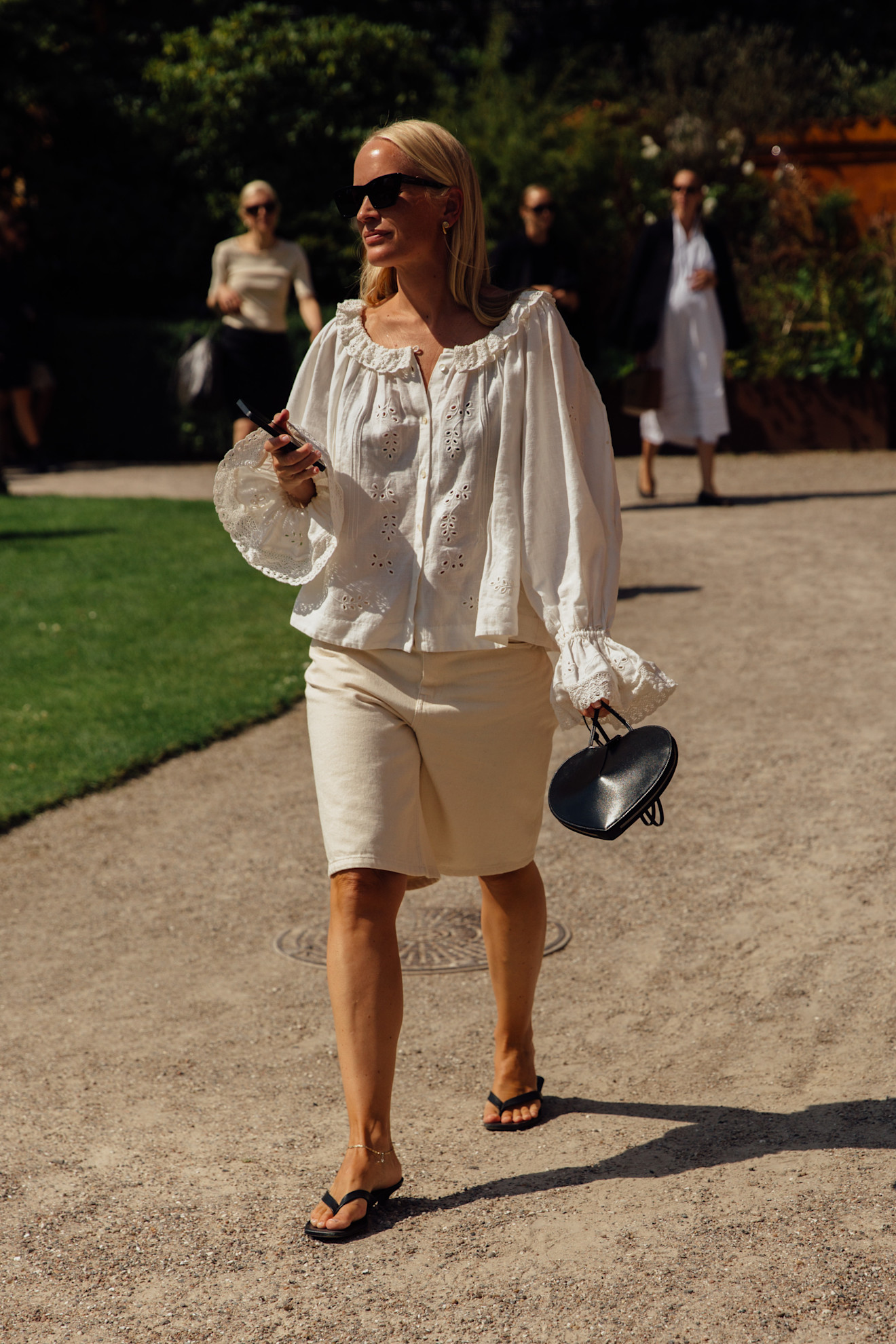 a fashion week attendee wearing sunglasses, white blouse, white denim shorts, and flip flops