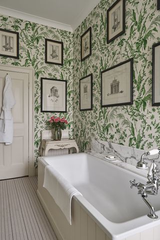 An example of green bathroom ideas showing a traditional bathroom with botanical green wallpaper and artwork on the walls