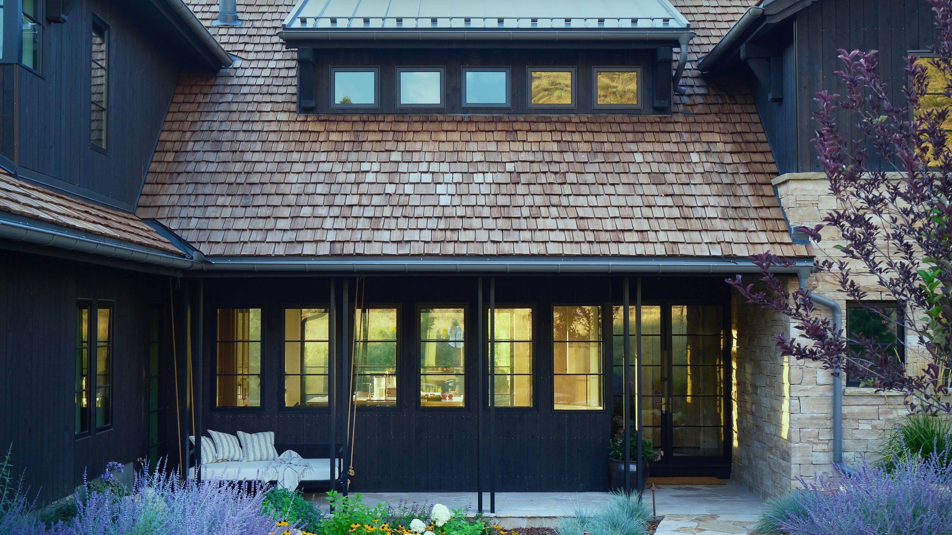 Exterior of a dark wooden clad house with a shingle roof and a landscaped garden in front