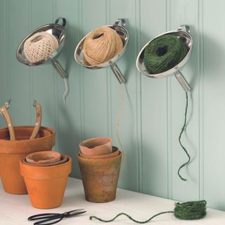 string in metal funnels attached to the a green panelled wall with terracotta pots on table below