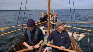 Four people row a recreation medieval era Norse ship.