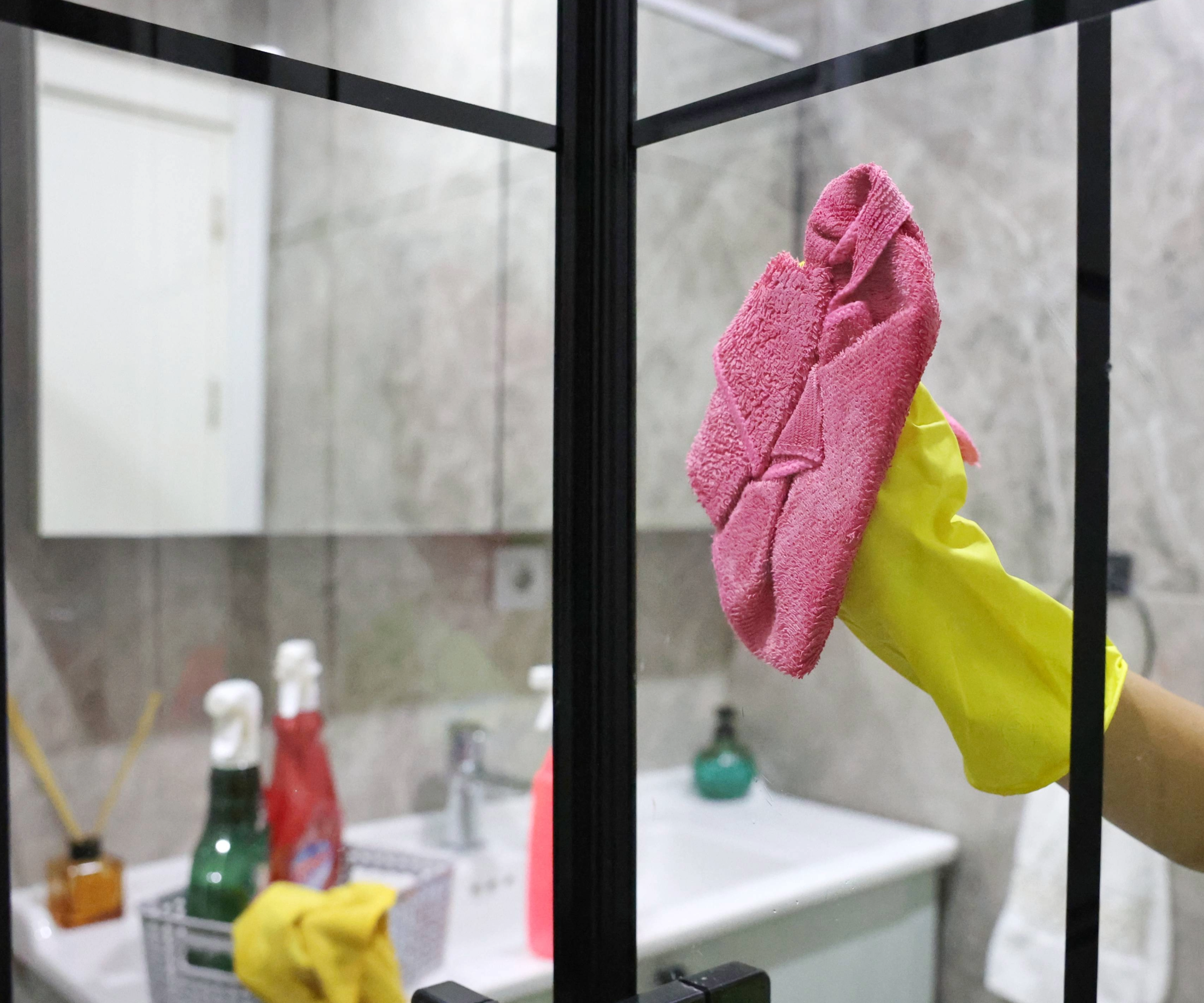 Rubber gloved hand cleaning shower screen