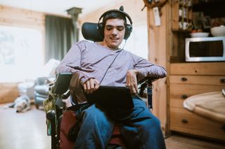 A disabled student is sitting a wheelchair listening to music.