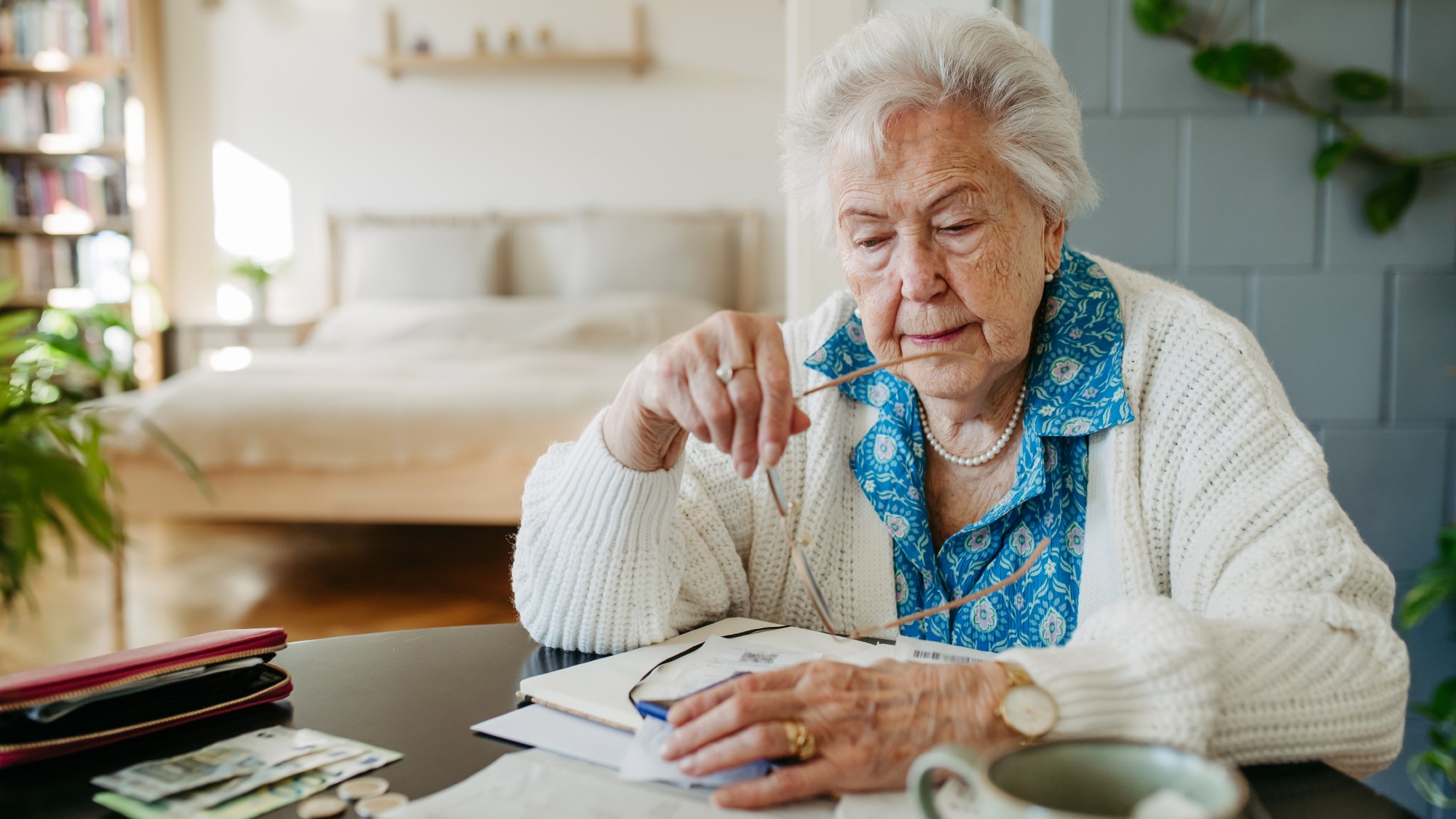 Senior woman sitting at living room table looking at financial bills