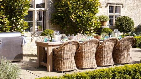 Summer garden with long wood table, woven seating on stone pavers, stainless steel barbecue