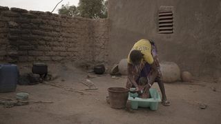 A woman bathes a baby in a small plastic tub in a barren outdoor yard.