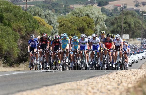 The peloton crest a hill beneath sunny skies in Australia.