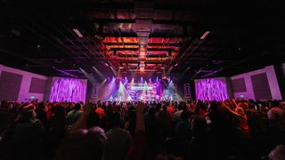 A house of worship's stage is illuminated in purple lights as a band rocks with L-Acoustics sound systems.