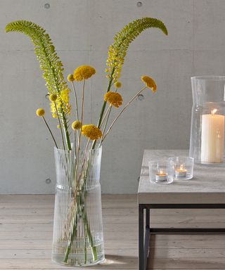Glass vase, yellow flowers in a vase, flowers in a home, flowers next to a candle