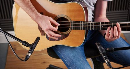 A man records a dreadnought acoustic guitar with a pair of condenser mics