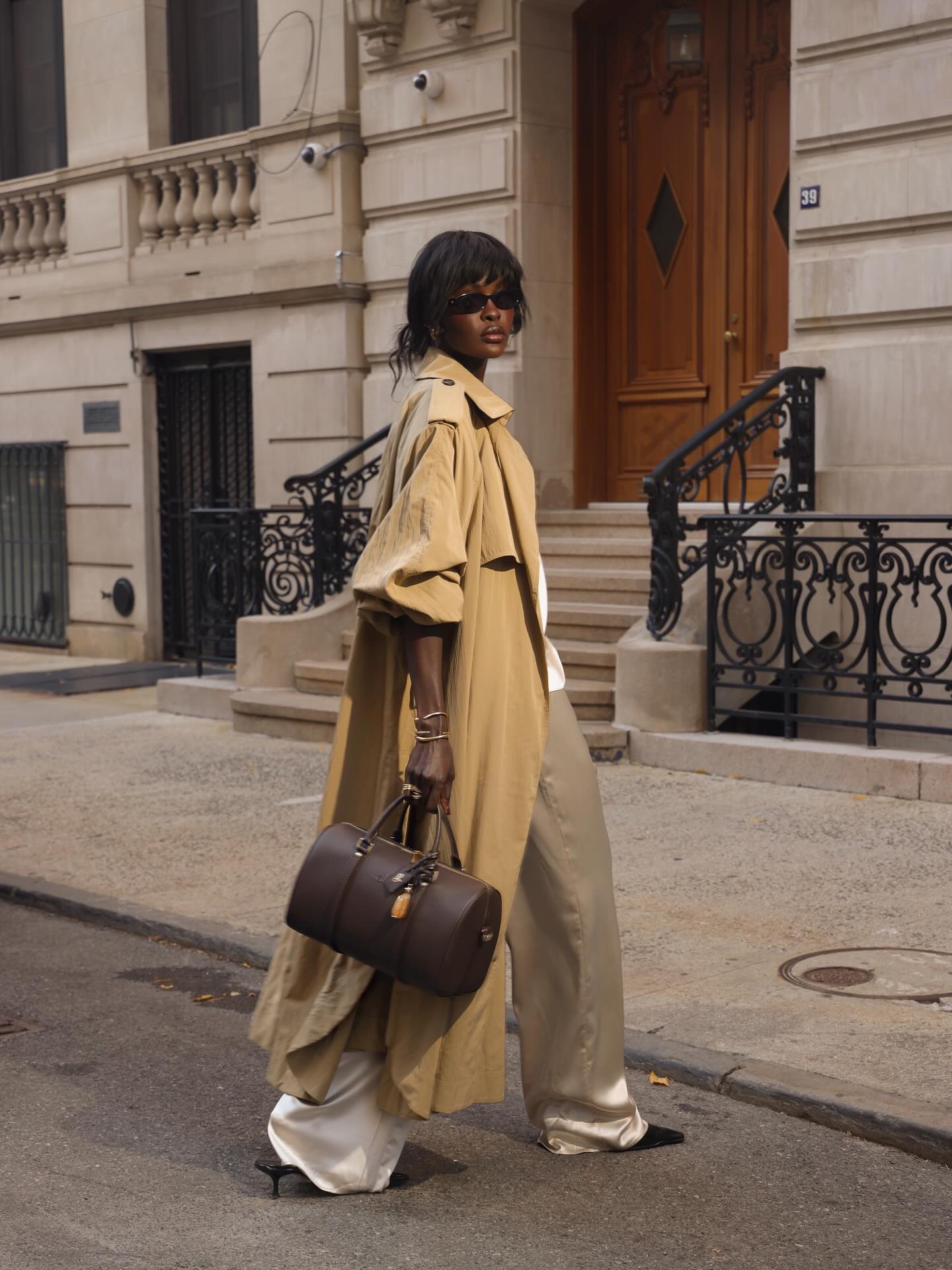 Woman wearing a long trench coat and satin trousers.