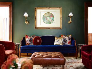 living room with green walls and blue velvet sofa with leather ottoman and artwork