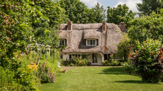 Thatched house surrounded by lush gardens