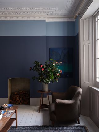 A living room with an armchair, a wood stack in the fireplace, and dark blue walls with the upper quarter painted light blue