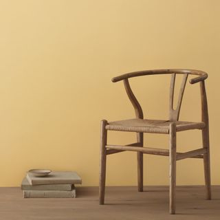 yellow wall with wooden floor, wooden chair, stack of books on the floor