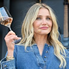 Cameron Diaz has long blonde hair, holds a wine glass, and wears a denim shirt