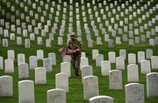 A U.S. soldier places American flags at the headstones at Arlington National Cemetery.