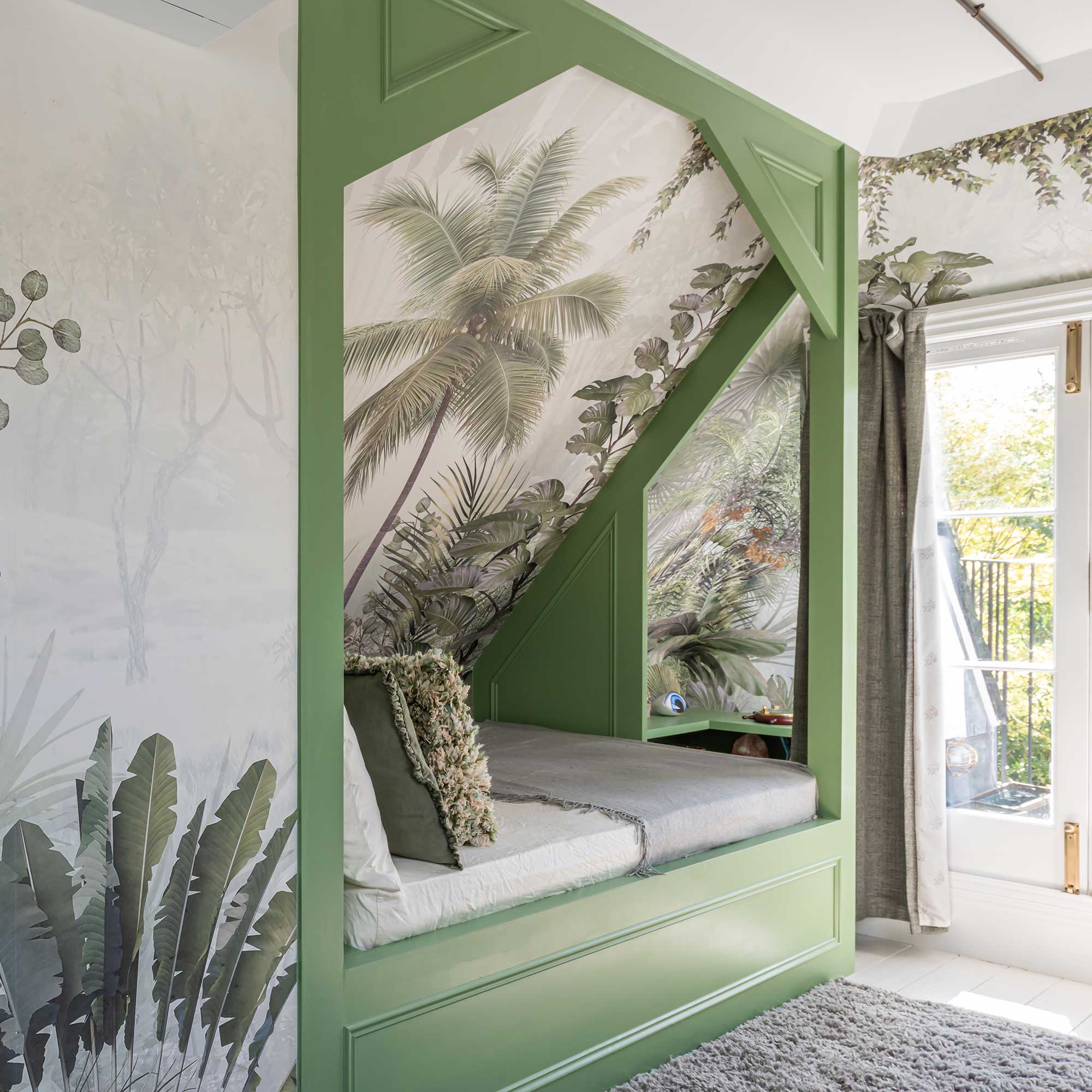green painted cabin bed built into sloping wall with botanical wall mural