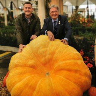 men with jacket and blazer posing with gaint pumpkin