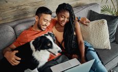 Shot of a young couple sitting with their Border Collie in their living room at home and using a laptop 