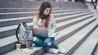 Best laptop backpacks, a photo of a girl sat on steps working with a laptop backpack