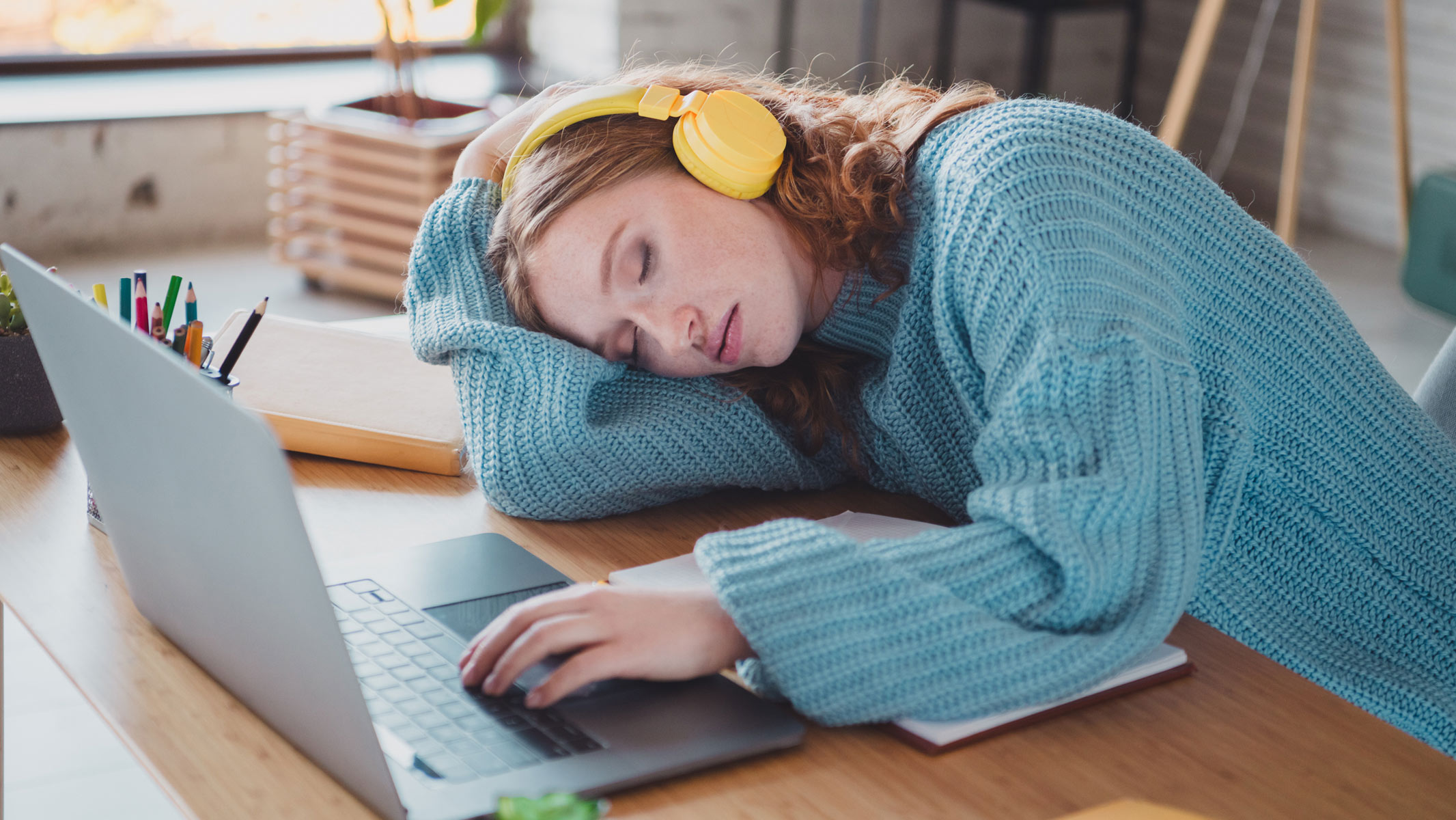 A young woman napping in front of a laptop while wearing headphones