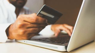 A person holding a credit card while typing on a computer