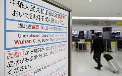 NARITA, JAPAN - JANUARY 17: A passenger walks past a notice forpassengers from Wuhan, China displayed near a quarantine station at Narita airport on January 17, 2020 in Narita, Japan. Japan's