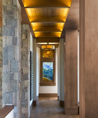A hallway with wooden ceiling, natural stone walls and an internal stained glass window at one end
