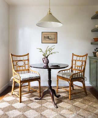 Simple breakfast nook with a small mahogany round table with two wicher dining chairs. A seagrass rug has been added beneath the seating area to add coziness and a built in green cabinet stores tableware and decor