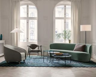 The curved green velvet Gubi sofa in front of large windows in a high-ceilinged period property