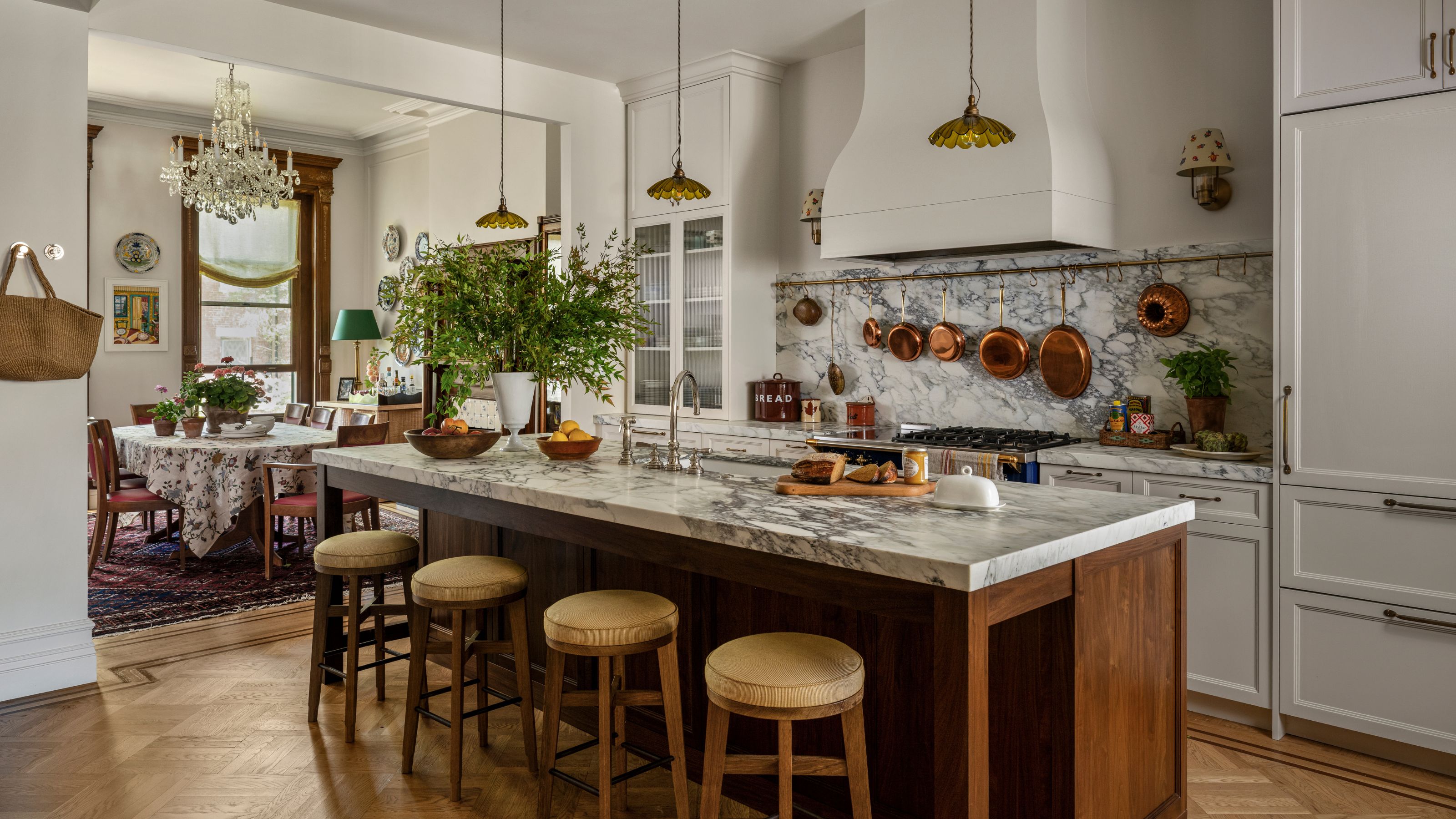 a new york brownstone kitchen with white cabinetry and a wooden island with marble counter and small vintage style pendants