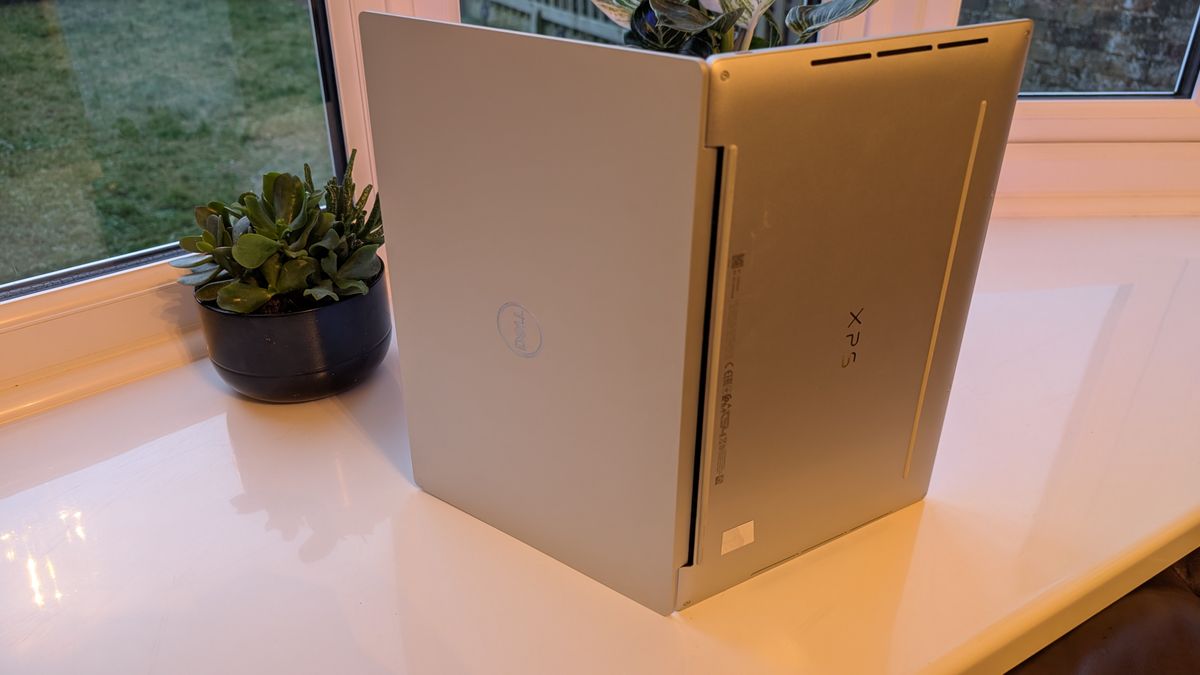 The Dell XPS 13 pictured on a white surface in front of a window with two potted plants.