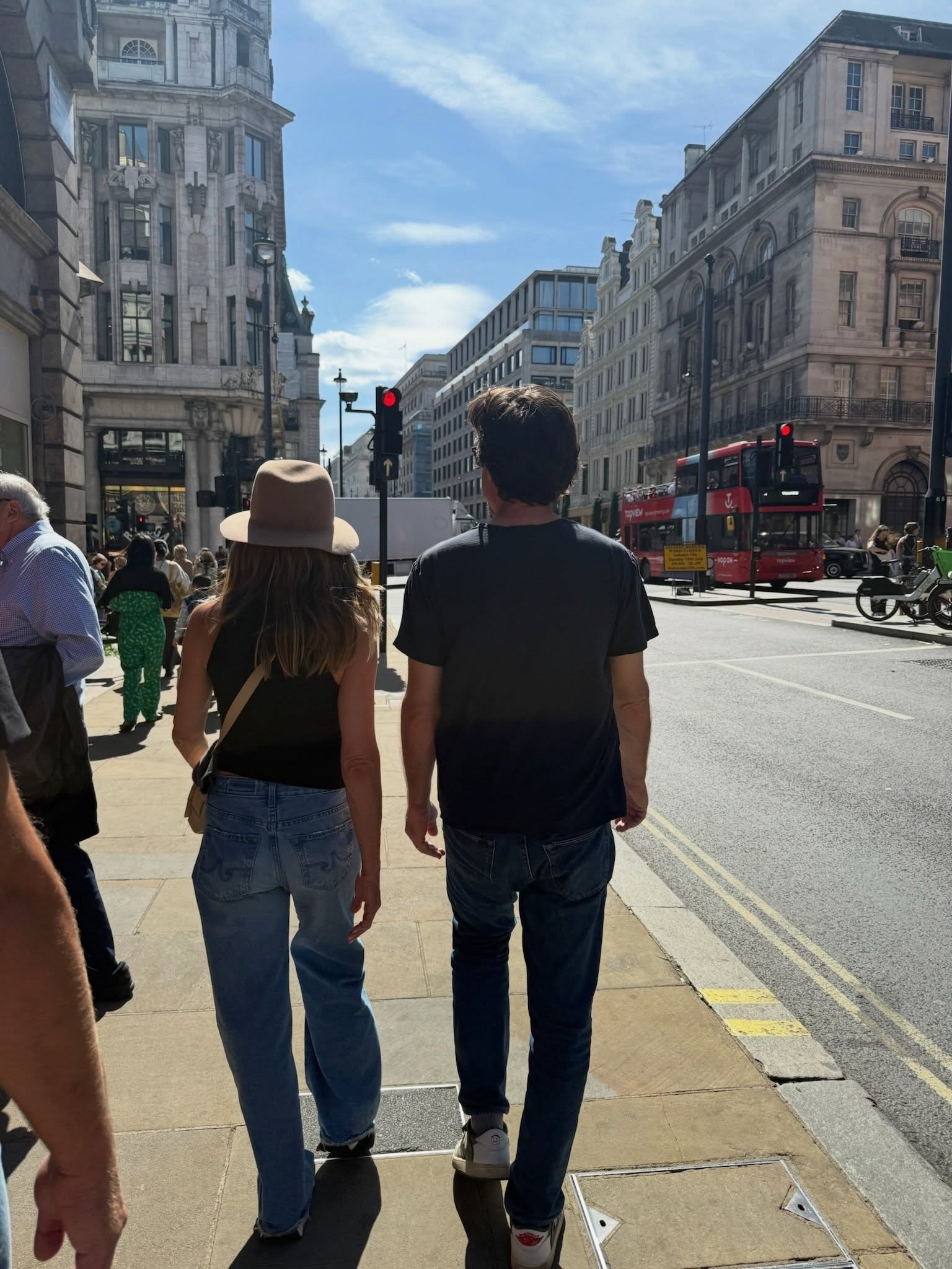 A view of Jennifer Aniston from behind in London, wearing AG jeans, a black tank top, and a hat.