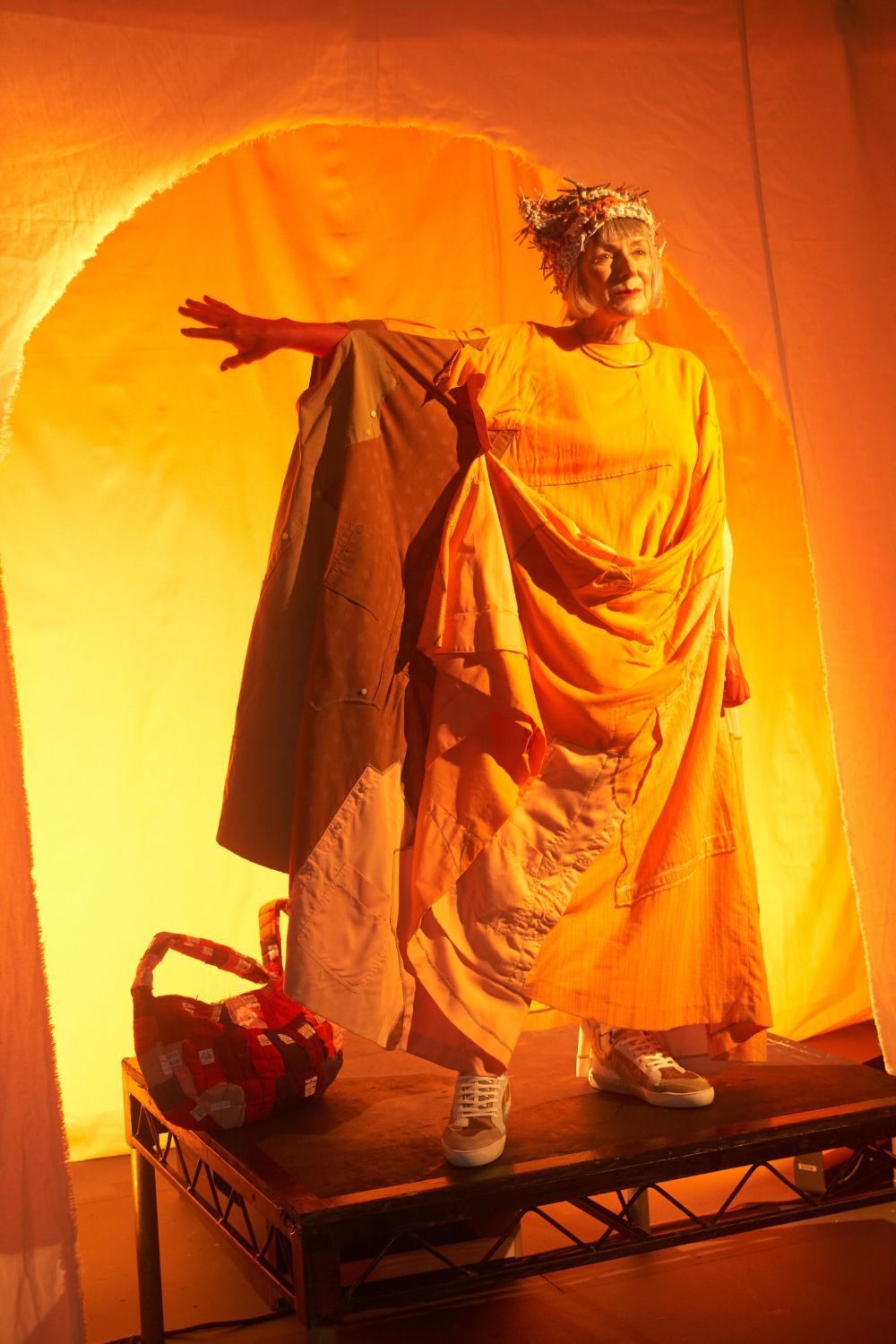 woman wearing orange dress holding her arm up on an orange backdrop