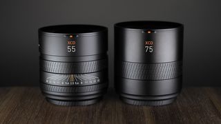 Hasselblad XCD 55V and 75P lenses side by side, on a wooden surface against a dark background