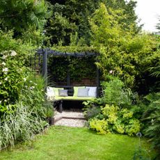 Pretty garden, grass lawn, black arbour frame, bench seating, cushions