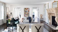 Large, open living room with ornate fireplace, two large doorways, a patterned rug, a green sofa,a gray sofa, two chairs and abstract art on the wall, on wooden floor with white walls and ceiling.