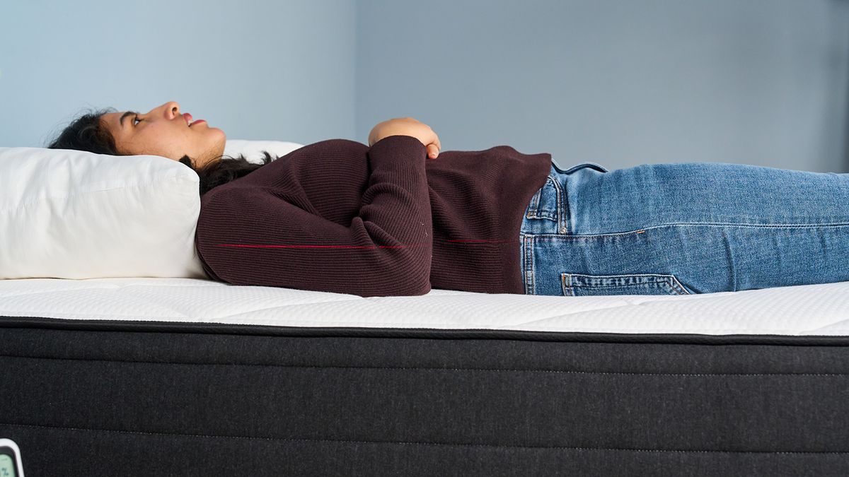 Mattress tester Becky George lies on her back on the Plank Firm Luxe mattress. A red laser line can be seen running along the center of the body, indicating her spine is being held straight.
