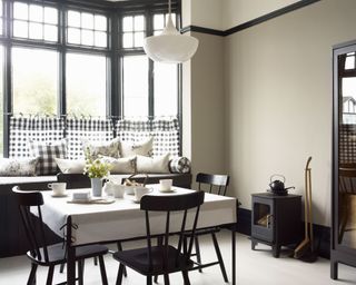White dining room with large bay window, monochrome check cafe curtains, window seating with cushions, small table, black dining chairs, pendant light, wood burning stove, Sabrina kettle on stove, dust pan and brush.