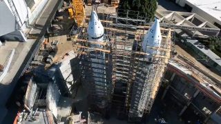 an aerial view of two white rockets surrounded by scaffolding and trees