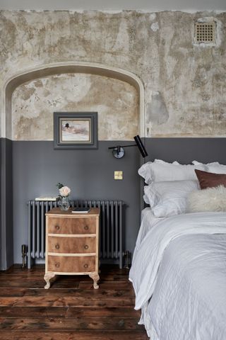 Bedroom with dark wood flooring, wood bedside table, and walls half plaster and half painted black