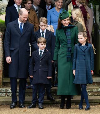 Prince William, Prince Louis, Prince George, Kate Middleton and Princess Charlotte wearing navy and green coats and ties for Christmas Day standing in front of church steps surrounded by other members of the Royal Family