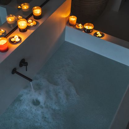 Aerial view of a rectangular bath filling with water and bubbles surrounded by candles in the top left corner