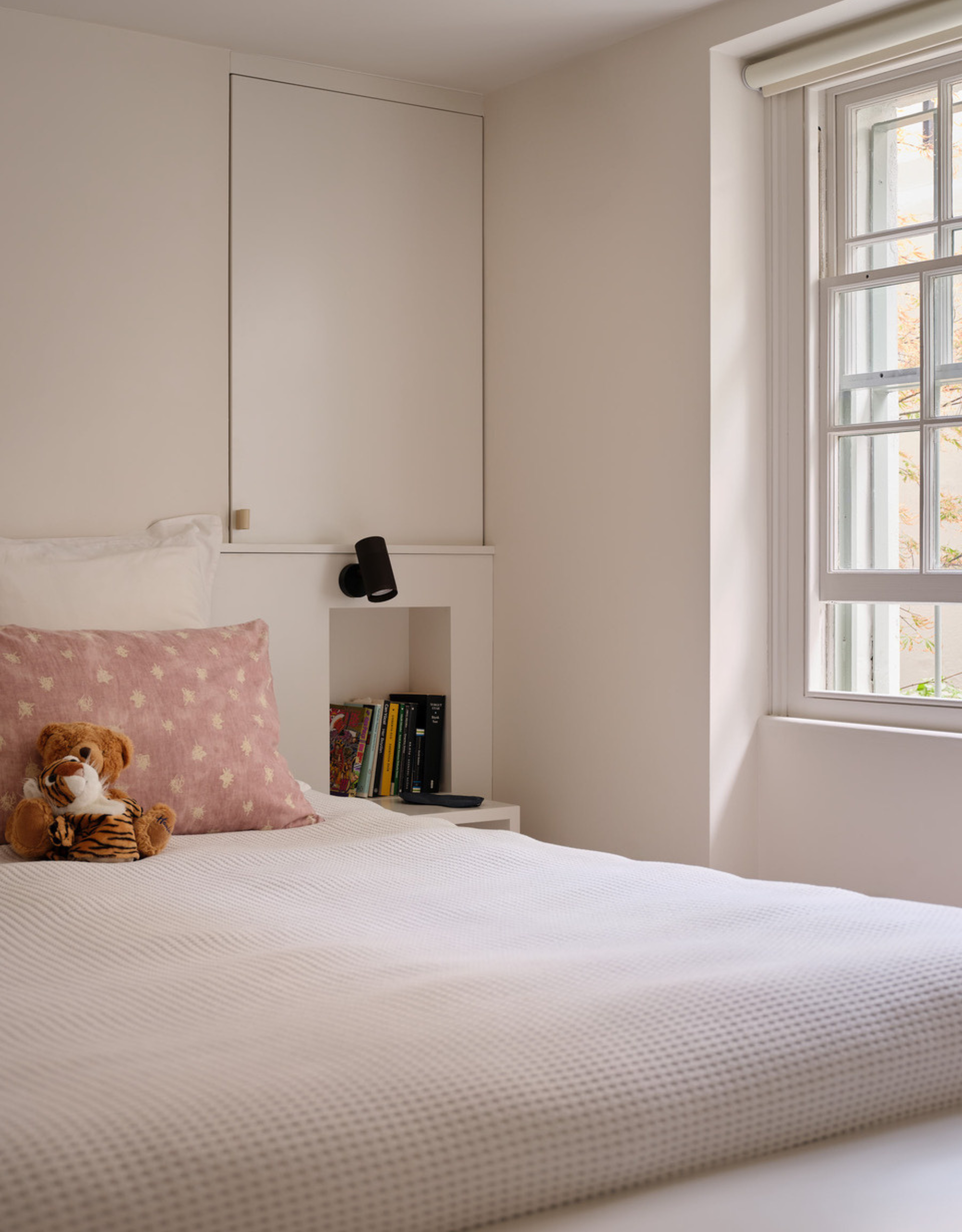 A bedroom with white walls, a minimalist bedscape, a stuffed toy, and a patterned pillow