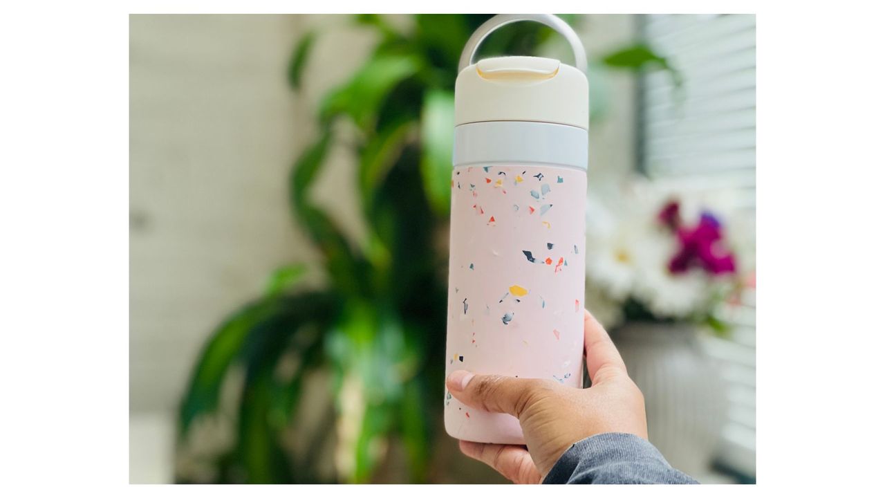A person holding a light pink speckled W&amp;P Porter Drink Through Insulated Bottle, for the best coffee travel mugs.