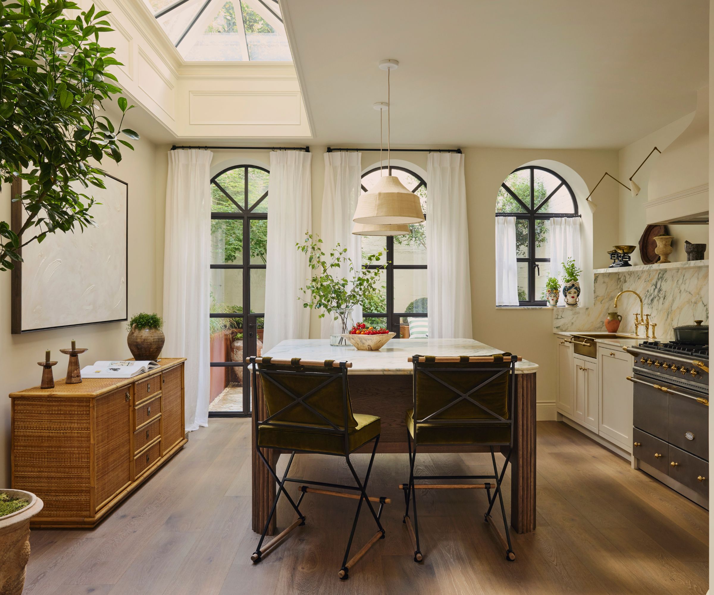 A neutral kitchen with a wooden freestaninf island, marble countertops, arched windows, and antique decor
