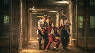 Arthur Fleck (Joaquin Phoenix) in full Joker makeup being dragged away by prison guards in Joker: Folie a Deux