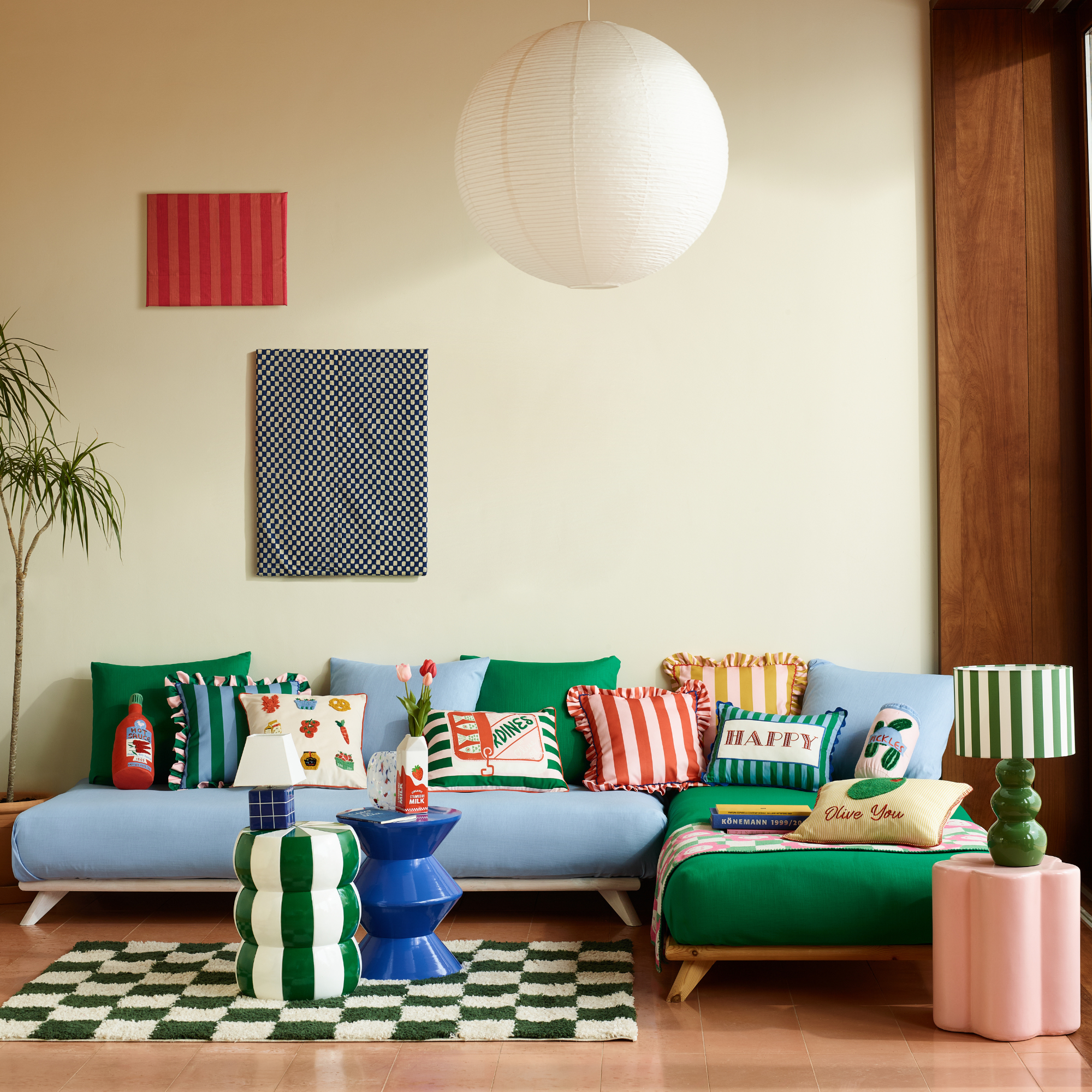 George Home new collection featuring lots of blue and green striped homeware positioned on a blue sofa in a modern living room.