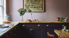 Farrow & Ball kitchen with a pink wall and dark purple cabinetry with wooden worksurface and rustic wood dining table and chair